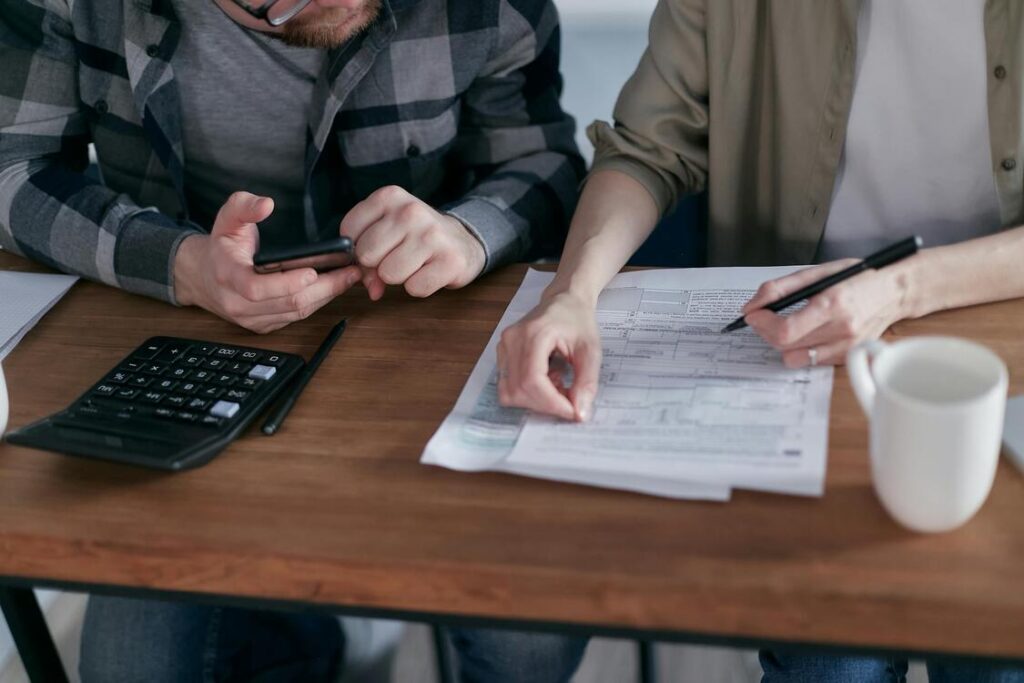 Duas pessoas na mesa, com calculadora e papeis, resolvendo as dívidas.